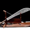 A Guandao Chinese Polearm weapon, with its scimitar sword and handle attachment leaning against a small wooden stand, along with the weapon's leather scabbard below on the floor.