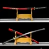 A decorated gold and white dragon sword Katana shown both sheathed and displayed crossed against its red scabbard, on a wooden sword-stand.