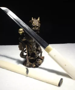 A JapaneseTanto knife leaning against a small wooden statue, with its wooden sheath below on the floor.