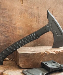 A tactical fighting tomahawk displayed standing balanced on a slab of wood, along with its axe scabbard below.