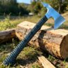 A fighting tomahawk axe, displayed leaning against a wood log, with a forest and field background.