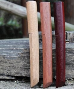 Three wooden Tanto Knives of differing wood-color, displayed side-by-side against a rock.