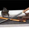 A modern Wakizashi sword displayed leaning against a small wooden sword-stand, with its scabbard below on the floor.
