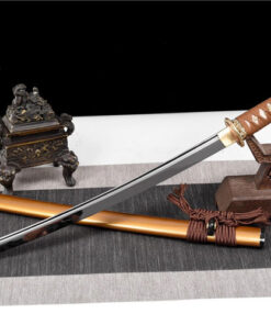 A modern Wakizashi sword displayed leaning against a small wooden sword-stand, with its scabbard below on the floor.