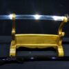 A one handed Japanese sword Wakizashi, displayed on a wooden sword-stand, with its black scabbard below on the floor.