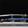 A champion sword Katana displayed next to its blue scabbard, on a small plastic sword-stand.
