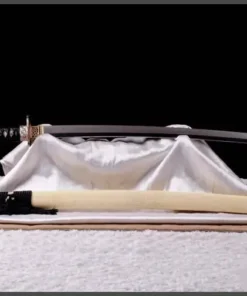 A black and white custom Katana sword, displayed on a white sheet, with its scabbard below on the floor.