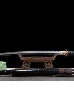 A custom made Katana displayed on a small wooden sword-stand, with its black scabbard below on the floor.