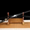 A black dragon sword and its scabbard, displayed on a small wooden stand.
