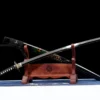 A mirror blade display sword, displayed crossed against its decorative scabbard, leaning against a small wooden sword-stand.