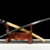 A decorated eagle sword Katana, displayed next to its engraved scabbard, leaming against a small wooden stand.