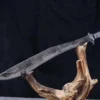 A full tang Kukri sword weapon, displayed balanced on a wood log branch.