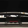 A Katana sword black and white in color, displayed next to its scabbard, on a small wooden stand.