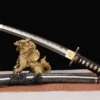 A dragon Tanto knife displayed leaning against a small statue, with its sheath below on the floor.