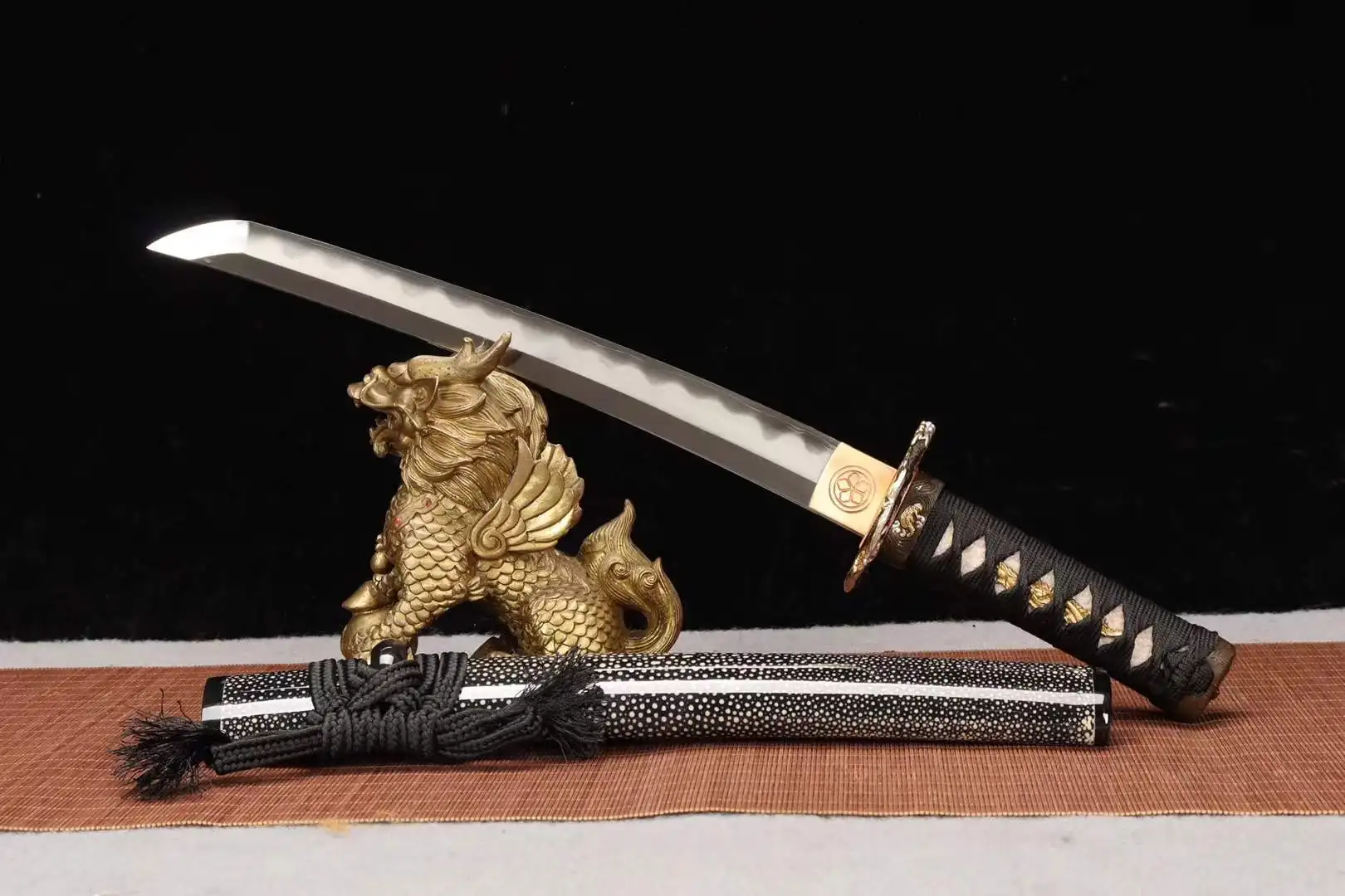 Dragon Tanto A dragon Tanto knife displayed leaning against a small statue, with its sheath below on the floor.