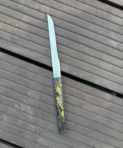 A small Kogatana knife, displayed lying on wooden floorboards.