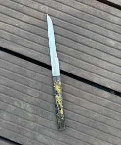 A small Kozuka knife, displayed lying on wooden floorboards.