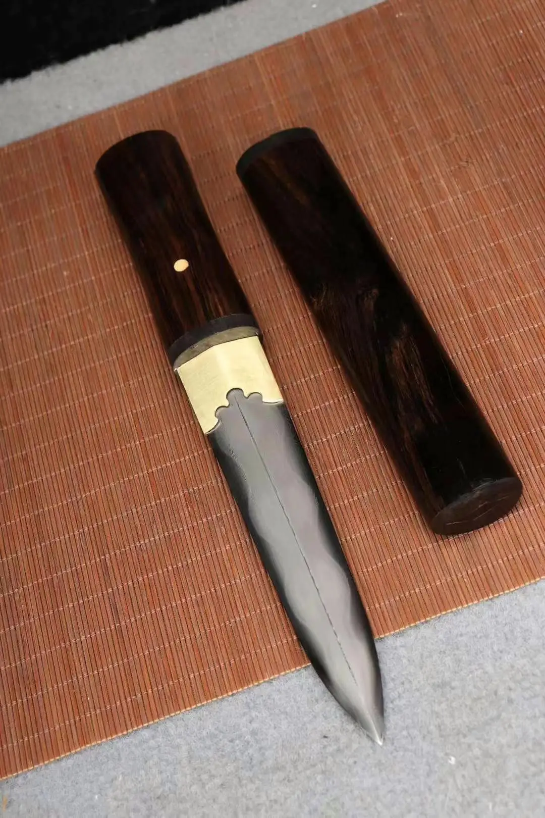 Mini Tanto A mini Tanto knife presented in Shirasaya, displayed next to its wooden sheath, lying on a bamboo mat.