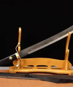 A short curved sword saber, displayed leaning against a small wooden stand, with its scabbard below on the floor.
