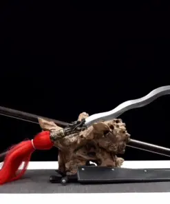 A sepent snake spear displayed next to its pole handle extension, leaning against a small wood log.