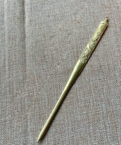 A Kogai Japanese hair pin made of brass, displayed lying on a hessian mat.