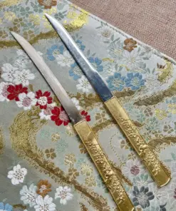 Two Japanese Kogatana knives displayed side-by-side on a decorative silk cloth.