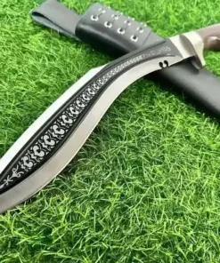 A tactical Kukri weapon displayed lying against its sheath on green grass.