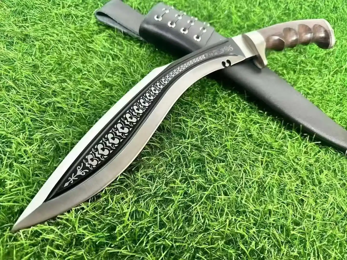 Kukri Weapon A tactical Kukri weapon displayed lying against its sheath on green grass.
