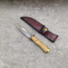 A Damascus hunting knife, displayed next to its leather sheath,