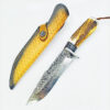 A Damascus survival knife displayed nest to its leather sheath.