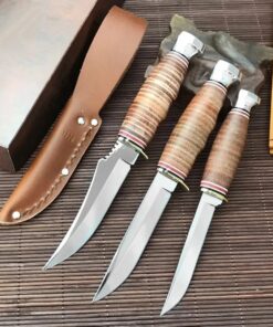 Three fixed blade hunting knives displayed next to a leather knife sheath.