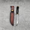 A Damascus hog hunting knife, displayed next to its leather sheath.