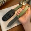 A mans hand holding a Nessmuk pig skinning knife, with the same knife shown sheathed, lying on a table.