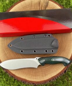 A fixed blade survival hunting knife, displayed next to its Kydex sheath and box on a tree stump.