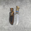 A survival knife with a Damascus steel fixed blade, displayed next to its leather sheath.