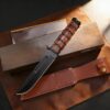 A marine usmc knife displayed next to its leather sheath and box.