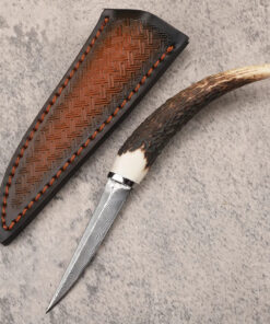 A deer antler handle knife displayed next to its leather sheath.