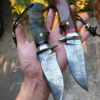 A hand holding two Damascus blade knife models.