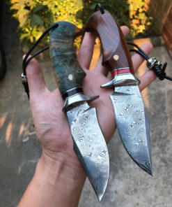 A hand holding two Damascus blade knife models.