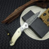 A Damascus folding pocket knife, displayed leaning against a small black box.