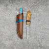 A fixed blade Damascus knife, displayed next to its leather sheath.