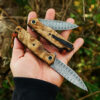 A hand holding a Damascus pocket knife with clip.