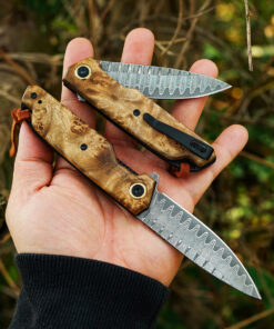 A hand holding a Damascus pocket knife with clip.