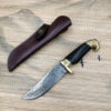 A Damascus steel skinning knife, displayed next to its leather sheath.
