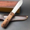 A wood handle fixed blade knife, displayed leaning against a box and its leather sheath.