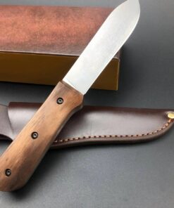A wood handle fixed blade knife, displayed leaning against a box and its leather sheath.