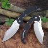 A big folding knife displayed leaning against some tree branches on a forest floor.