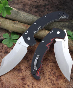 A big folding knife displayed leaning against some tree branches on a forest floor.