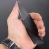 A man's hand holding a slim folding credit card knife.
