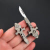 A man's hand holding a mini keyring knife multi tool.
